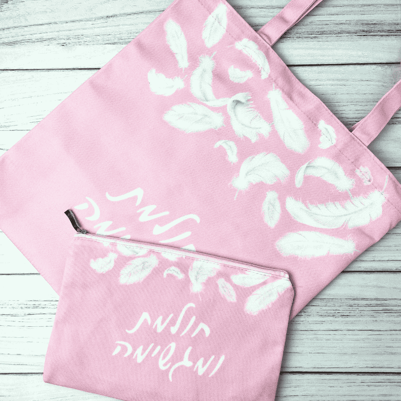 תיק קנבס דגם חולמת ומגשימה כיתוב בצבע לבן תיק בצבע ורוד ברקע נוצות לבנות