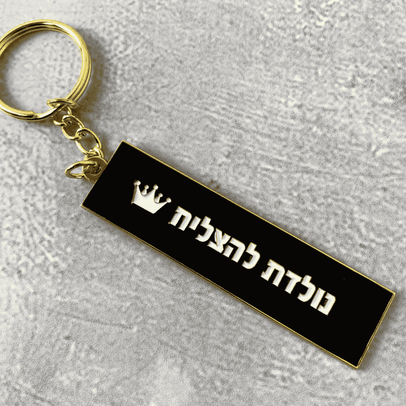 מחזיק מפתחות מוזהב דגם נולדת להצליח כיתוב בצבע לבן עם כתר לבן רקע שחור