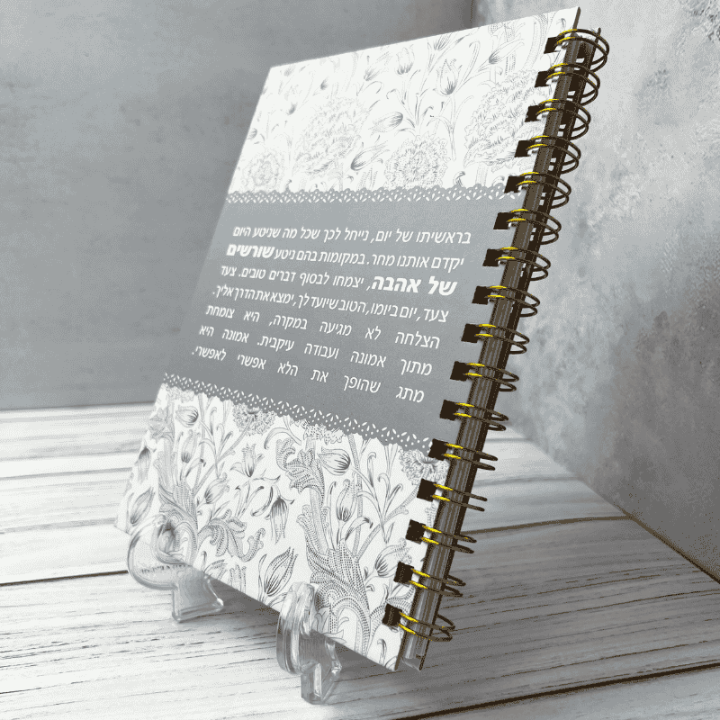  מחברת כריכה קשה דגם הצלחה צומחת מתוך אמונה עיצוב של פרחים שחורים על רקע לבן עם באמצע פס עבה אפור תכלת עם הכיתוב ספירלה מוזהבת